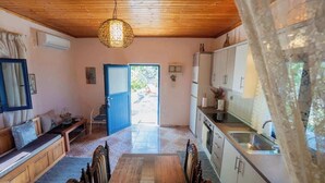 A room with a wooden ceiling, a dining table with chairs, a kitchen area with cabinets, and a door leading outside. - Irene's Cottage Myrtonas | Hilltop Sea View Retreat (Karpathos)