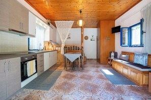 A kitchen with wooden cabinets, a dining table with chairs, a bench, and a TV on the wall.