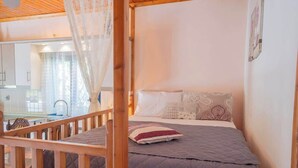 Une chambre à coucher avec un lit, une tête de lit en bois, une fenêtre avec des rideaux et une vue sur la cuisine.