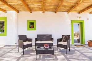 Un espace extérieur aménagé avec des meubles en osier, une table basse en verre et une plante en pot.