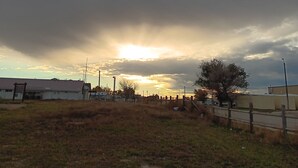 A rural landscape with a cloudy sky, a sunset, and a fence.