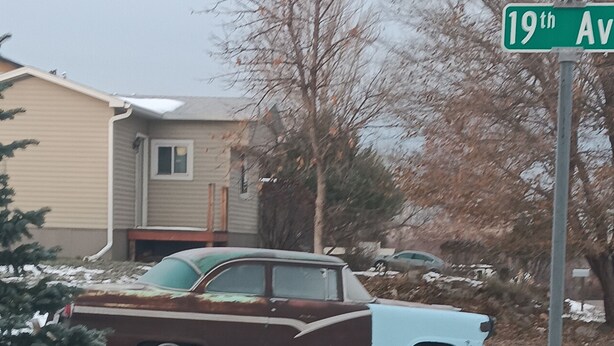 A vintage car parked on a snow-covered driveway, a house in the background, and a street sign indicating '19th Ave.'