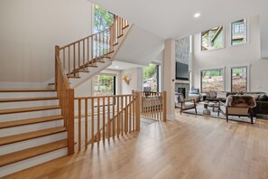 A spacious living area with a wooden staircase, a fireplace, and a view of the outdoors.