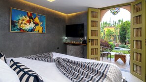 Ein Schlafzimmer mit Bett, einem Bild, einem Fernseher und einer offenen Tür, die in einen Garten führt.