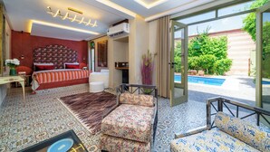 Ein Schlafzimmer mit Bett, Schreibtisch, Sessel und einer Couch, mit Blick auf einen Außenpool.