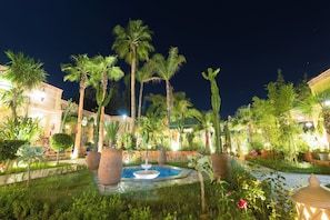 A nighttime garden with a fountain, palm trees, and potted plants. - Jnane Rihane Marrakech (Marrakech)