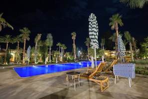 Ein Pool mit Liegestühlen und Sonnenschirmen, umgeben von Palmen und einem Sternenhimmel.
