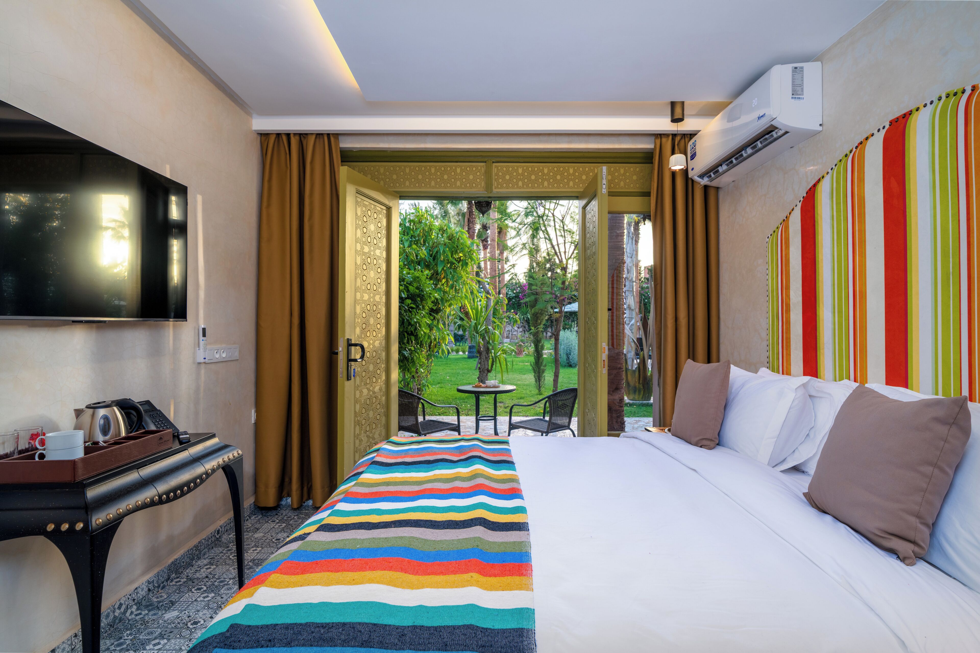 Een hotelkamer met een bed, een bureau, een televisie en uitzicht op een tuin.
