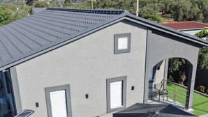 Ein modernes Gebäude mit flachem Dach, zwei Fenstern und einer Terrassenfläche mit künstlichem Rasen, einem Tisch, Stühlen und einem großen Sonnenschirm.