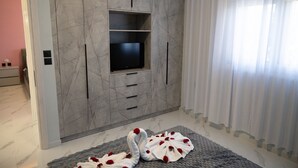 Ein modernes Wohnzimmer mit einem an einer Marmorwand montierten Flachbildfernseher, einem grauen Teppich mit roten Blumen und einem Fenster mit durchscheinenden Vorhängen.