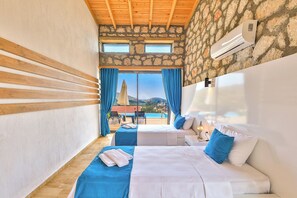 A hotel room with two beds, a stone wall, a wooden ceiling, and a view of a pool and mountains.