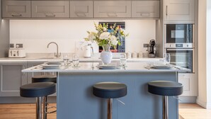 A modern kitchen with grey cabinets, a central island with stools, a vase with flowers, and a built-in oven. - Swift Apartments - Apartment 6 with Free Gym Access (York)