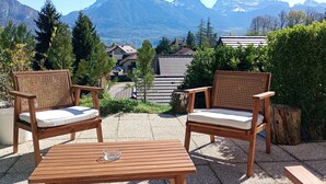 Zwei Korbstühle mit Kissen, ein Holztisch und im Hintergrund eine Aussicht auf Berge und Häuser.