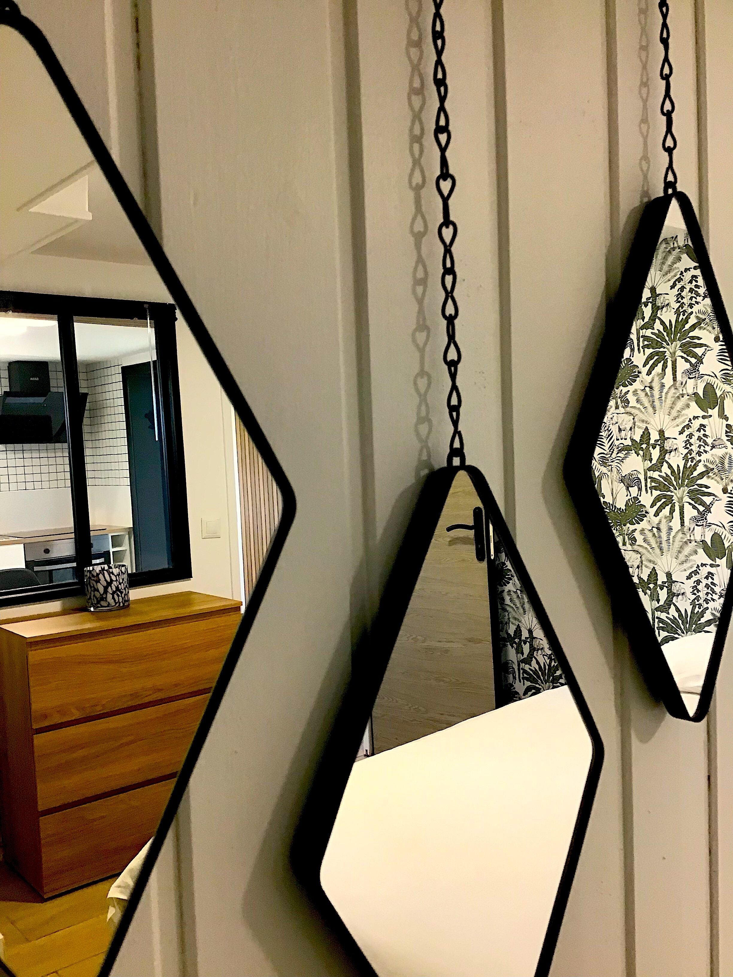 Une pièce comprenant une commode en bois, un miroir à cadre géométrique et un luminaire suspendu.