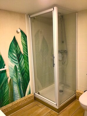 A glass-enclosed shower with a handheld showerhead, a tiled floor, and a wall with a large green leaf mural.