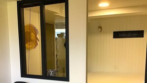 Ein Zimmer mit einem Holztisch, zwei schwarzen Stühlen, einem Bett mit weißem Kopfteil, einem Spiegel mit schwarzem Rahmen und einem Schild an der Wand.