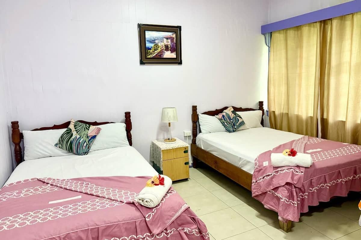 A hotel room with two beds, a nightstand, a framed picture on the wall, and a window with curtains.