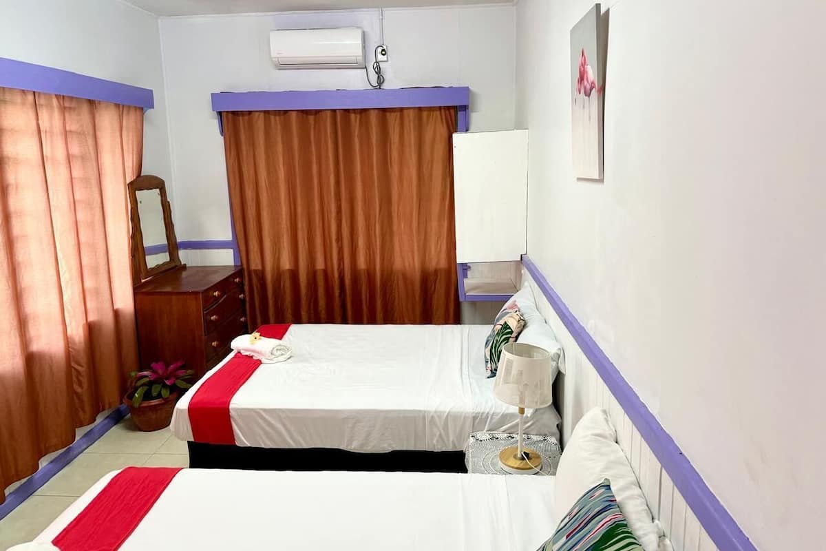 A hotel room with two beds, a dresser, a mirror, an air conditioning unit, and a window with curtains.