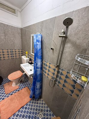 Ein Badezimmer mit Toilette, Waschbecken, Dusche und Fliesenboden mit Muster.