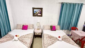 Una habitación con dos camas, una mesita, una silla, una lámpara y un cuadro en la pared.
