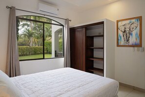 A bedroom with a bed, a window with curtains, a wooden wardrobe, and a painting on the wall.