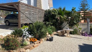 Ein Haus mit überdachter Auffahrt, einem Steinsschornstein und einem Garten mit verschiedenen Pflanzen und Blumen.
