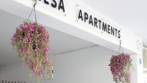 Entrada d'un edifici amb un cartell que diu 'ELSA APARTMENTS' i cistelles florals penjants.