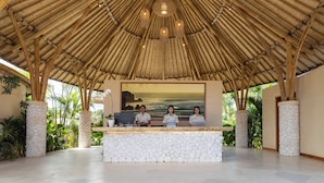 Zona de recepción con techo de bambú, un mostrador de recepción y un cuadro grande enmarcados de una playa.