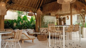 Un espacio de estar al aire libre con techo de paja, muebles de mimbre, barra y abundante follaje.