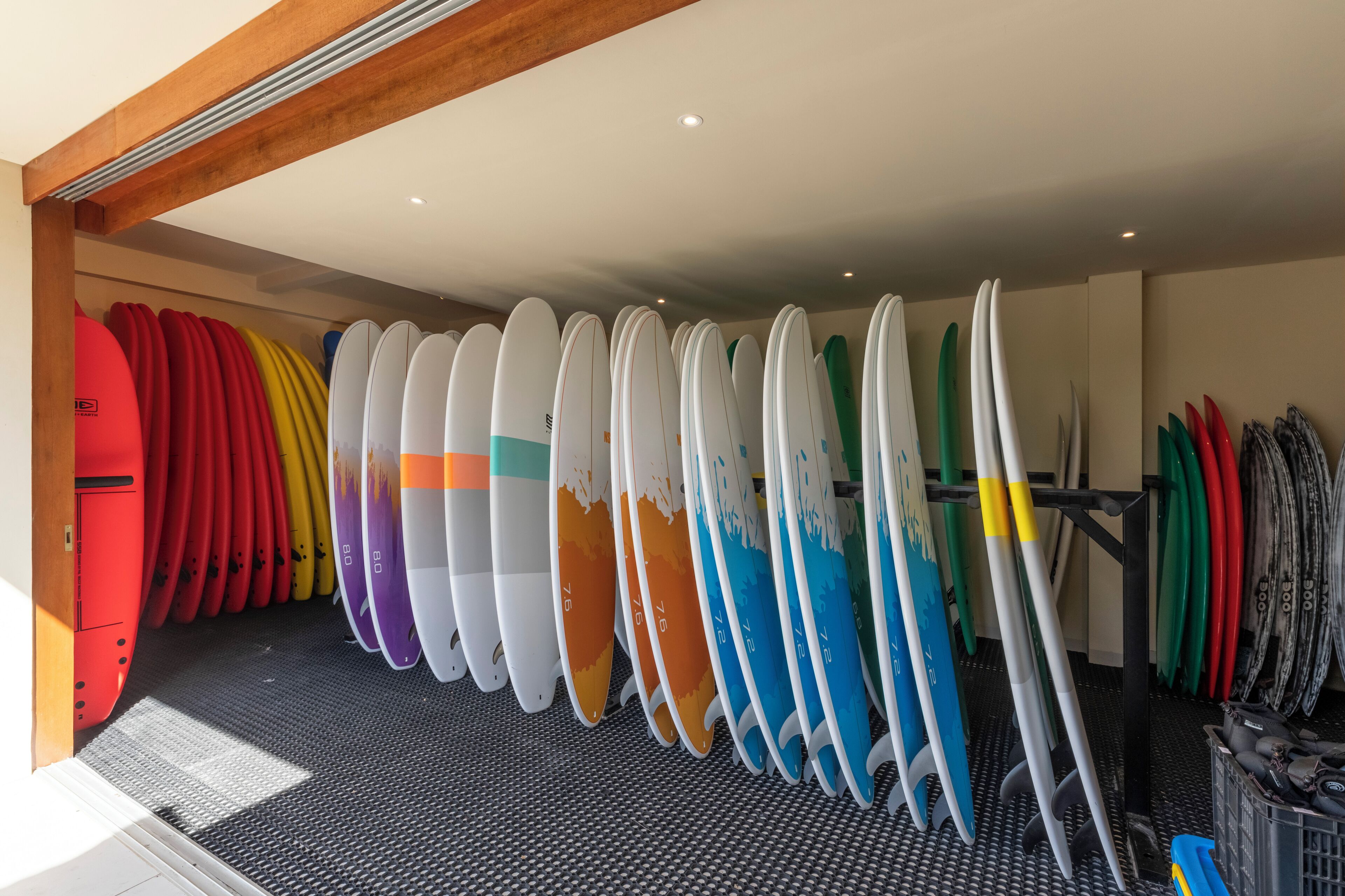 Varias tablas de surf en una habitación con piso negro y vigas de madera en el techo.
