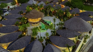 Un resort con construcciones de techo de paja, un edificio central y abundante vegetación.