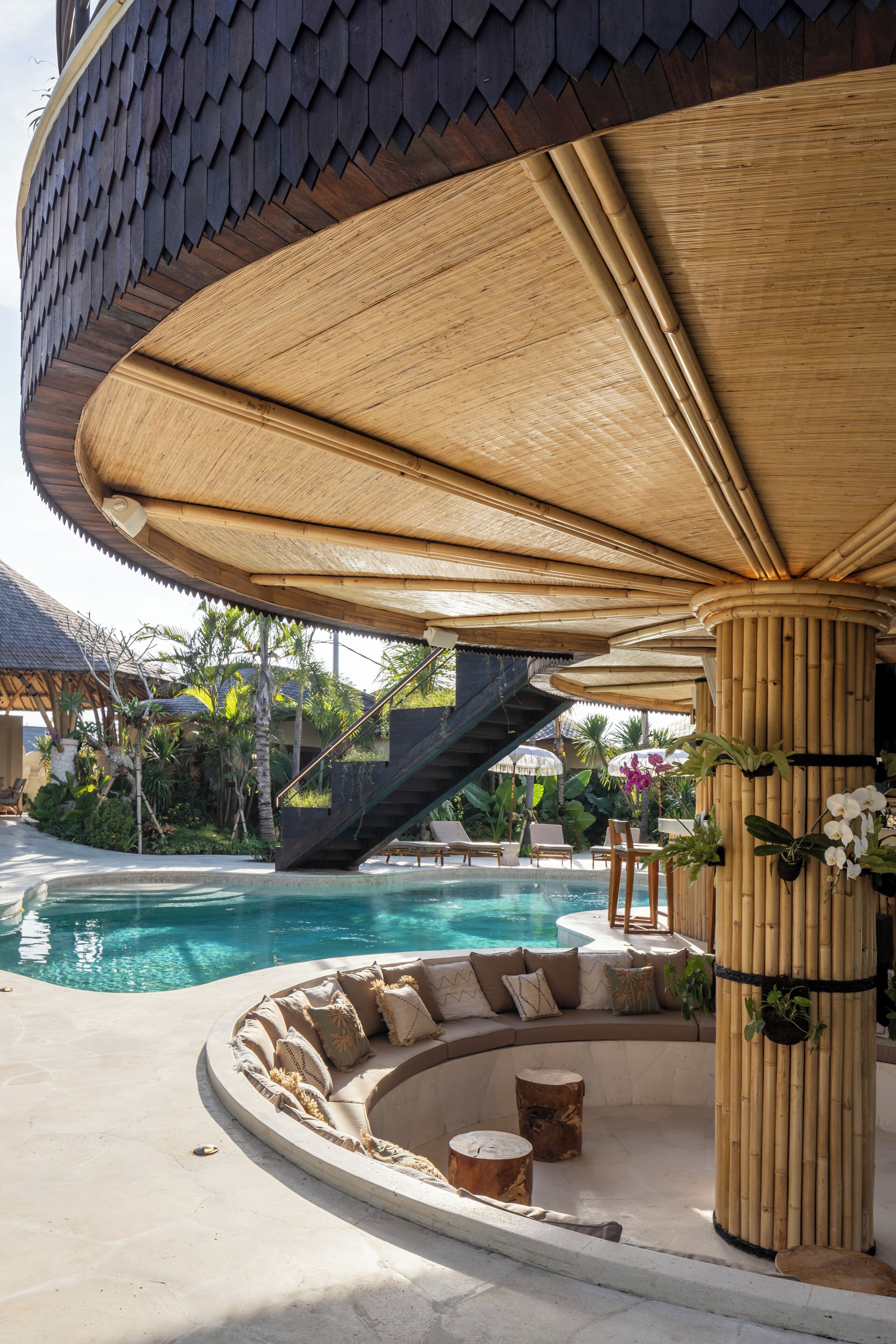 A pool area with a curved seating arrangement, a staircase, and a bamboo structure.