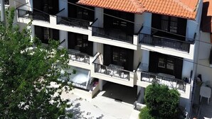 A multi-story building with a red-tiled roof, balconies, and a view of a green hillside. - Studio Apartment '3 with Sea View-for 3 Guests' with Sea View, Wi-Fi and Air Conditioning (Pefkochori)