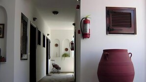 A hallway with a large red pot on wheels, a fire extinguisher, and a wall-mounted air conditioning unit. - Studio Apartment '3 with Sea View-for 3 Guests' with Sea View, Wi-Fi and Air Conditioning (Pefkochori)