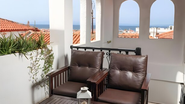 A balcony with two brown leather chairs, a small table with a white lantern, and a view of the sea through arched windows. - Studio Apartment '3 with Sea View-for 3 Guests' with Sea View, Wi-Fi and Air Conditioning (Pefkochori)