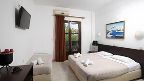 A hotel room with two beds, a flat-screen TV mounted on the wall, a painting, and a view of the outdoors through a window. - Studio Apartment '3 with Sea View-for 3 Guests' with Sea View, Wi-Fi and Air Conditioning (Pefkochori)
