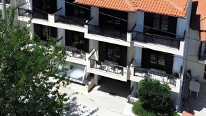 A multi-story building with a red-tiled roof, balconies, and a view of a green hillside. - Studio 'For 3 with Mountain View 4' with Shared Terrace, Wi-Fi and Air Conditioning (Pefkochori)