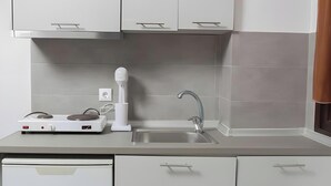 A modern kitchen with white cabinets, a built-in dishwasher, a sink, and a countertop with a kettle. - Studio 'For 3 with Mountain View 4' with Shared Terrace, Wi-Fi and Air Conditioning (Pefkochori)
