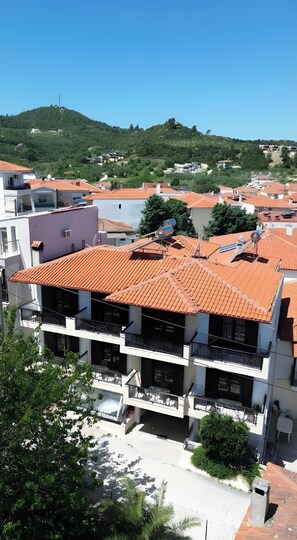 Un edificio de varios pisos con techo de tejas rojas, balcones y vistas a una ladera verde.