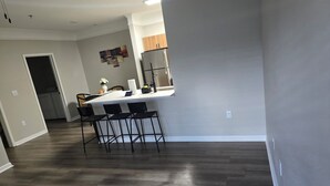 A modern kitchen with a white countertop, four bar stools, and a wooden cabinet above. - Elite Cozy Suites Buford (Buford)
