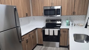 A modern kitchen with wooden cabinets, stainless steel appliances, and a white countertop. - Elite Cozy Suites Buford (Buford)