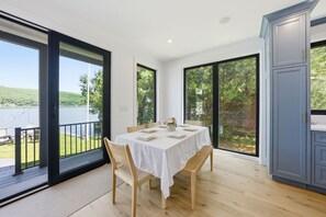Ein Essbereich mit Tisch für vier Personen, großen Fenstern und Blick auf einen See.