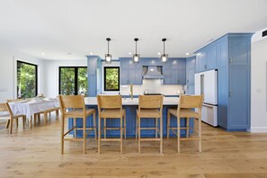 Uma cozinha moderna com armários azuis, uma ilha central com banquetas e iluminação pendente.