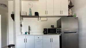 Una cocina moderna con armarios blancos, un refrigerador de acero inoxidable, un microondas y una cafetera.