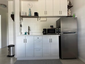 Eine moderne Küche mit weißen Schränken, einem Edelstahl-Kühlschrank, einer Mikrowelle und einer Kaffeemaschine.