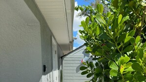 Un sendero estrecho de grava, un edificio blanco con una puerta y un arbusto verde.
