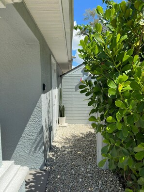 Ein schmaler Kiesweg, ein weißes Gebäude mit einer Tür und ein grüner Busch.