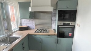 A kitchen with teal cabinets, a gas stove, a microwave, and a built-in oven. - Carnegie Library Christie apartment (Swinton)
