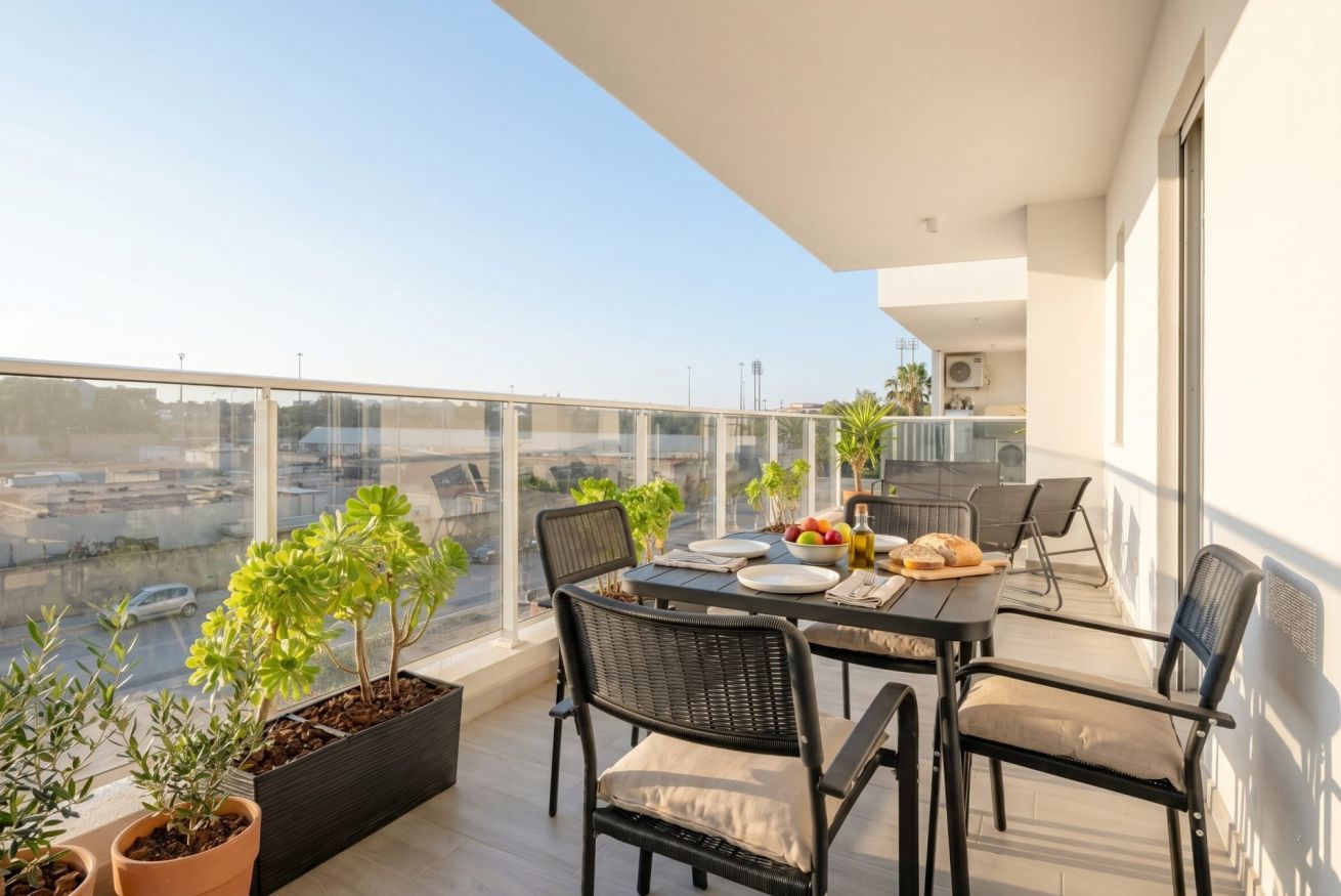 Un balcón con una mesa lista para comer, plantas en macetas y vistas de la ciudad.