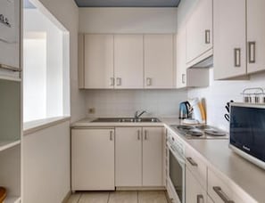 A compact kitchen with white cabinetry, a built-in oven, and a microwave. - Sea View Apartment for 6 in Zeedijk (Blankenberge)